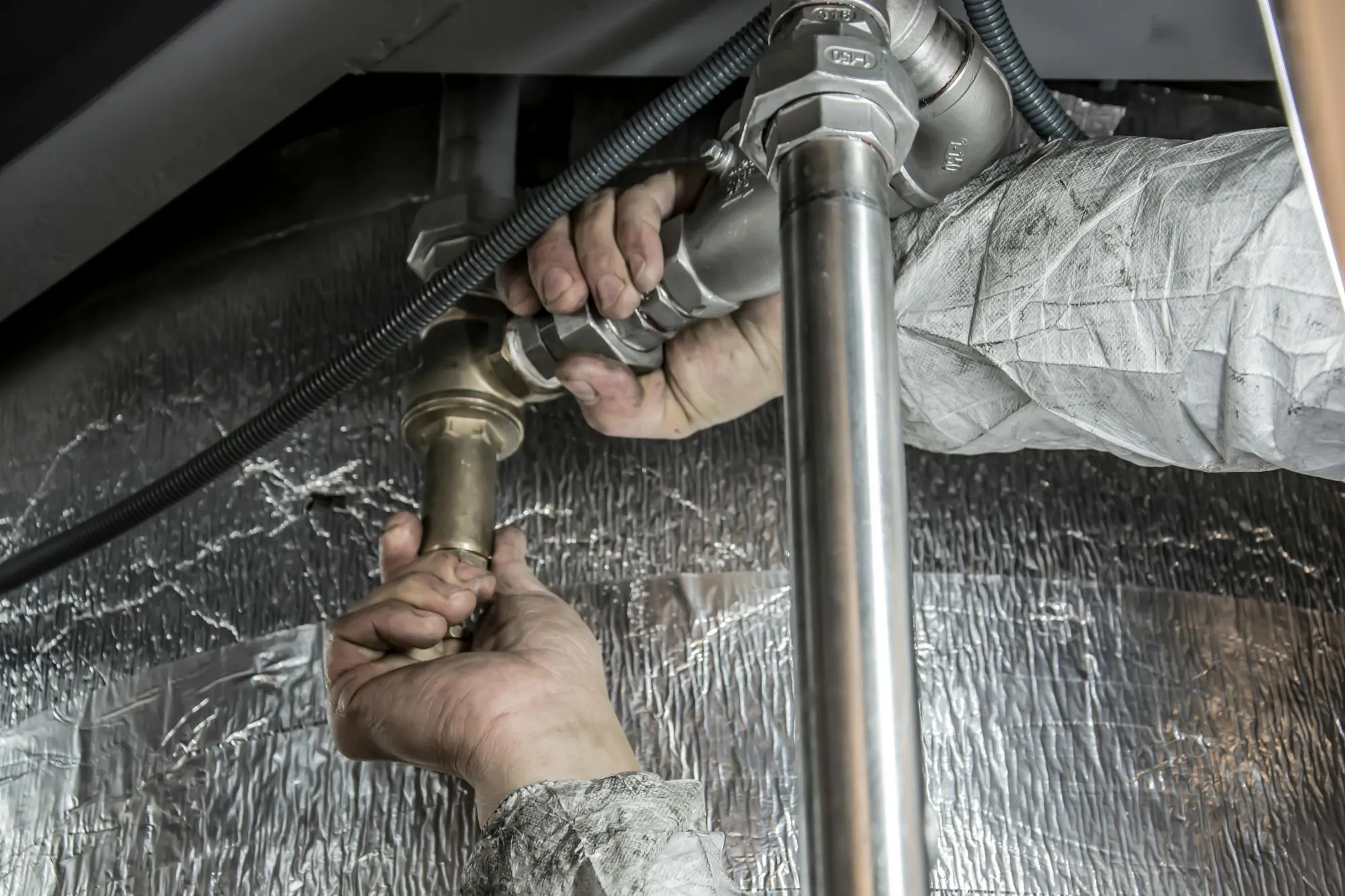 Plumber tightening a brass waste fitting under a stainless steel kitchen sink